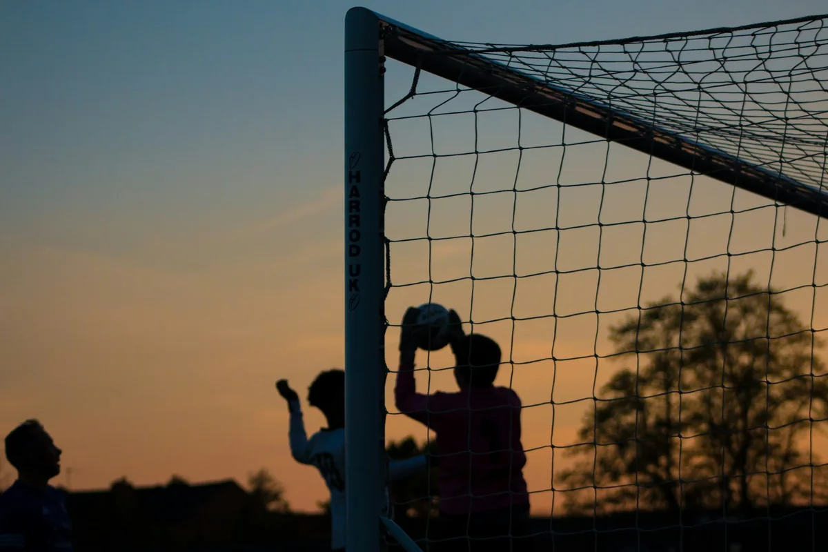 A goalkeeper catching a soccer ball at sunset